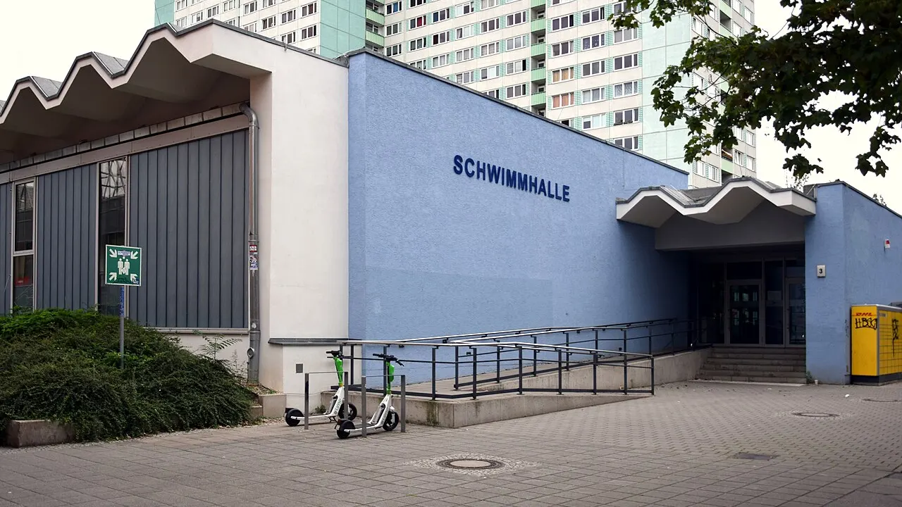 Blau verputzte Schwimmhalle Thomas-Mann-Straße in Berlin-Prenzlauer Berg mit dem Schriftzug Schwimmhalle, dahinter ein Wohnhochhaus