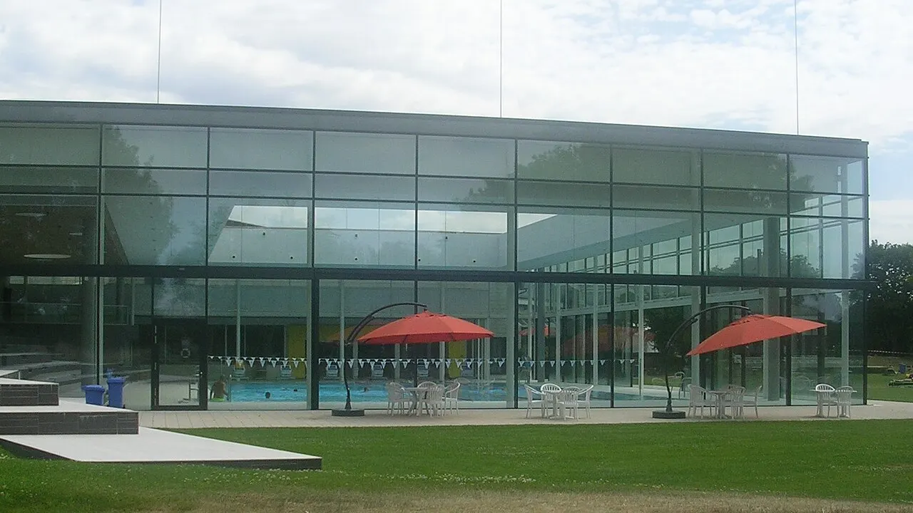 Glasfassade der Schwimmhalle des Fächerbads in Karlsruhe mit Liegewiese und roten Sonnenschirmen