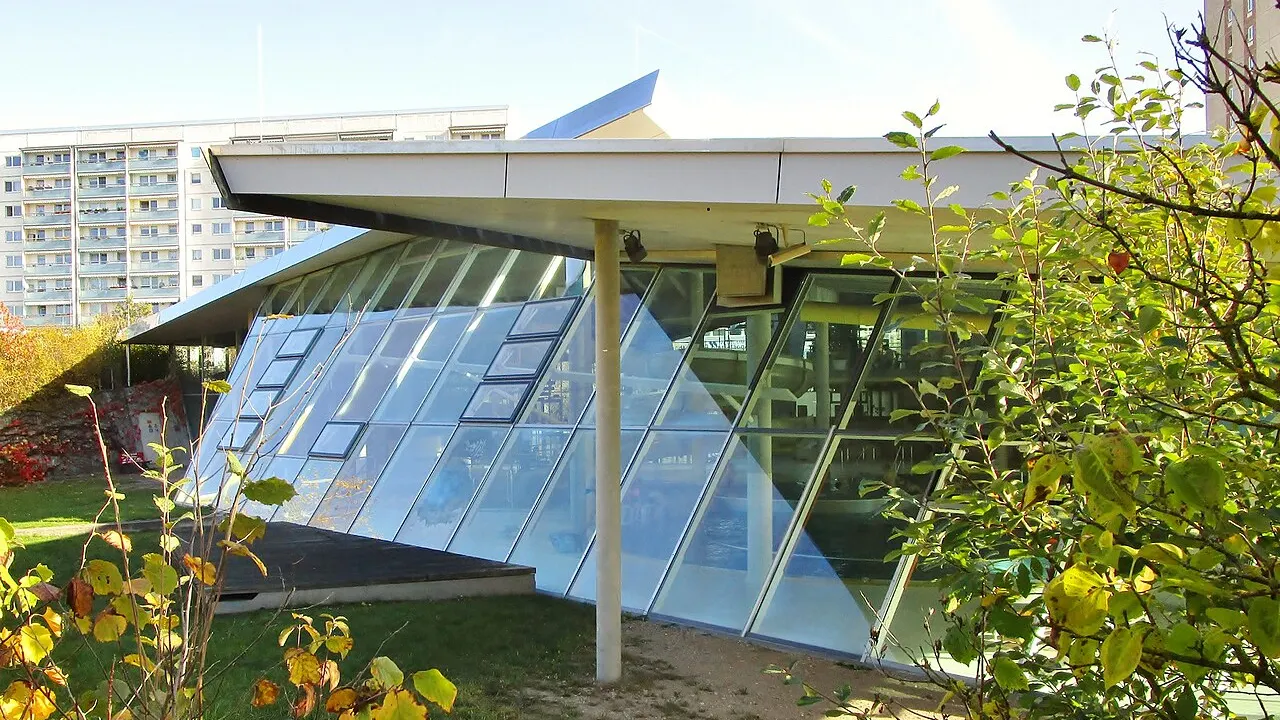 Schräge Glasfassade der Schwimmhalle Grünauer Welle in Leipzig-Grünau mit Plattenbauten im Hintergrund